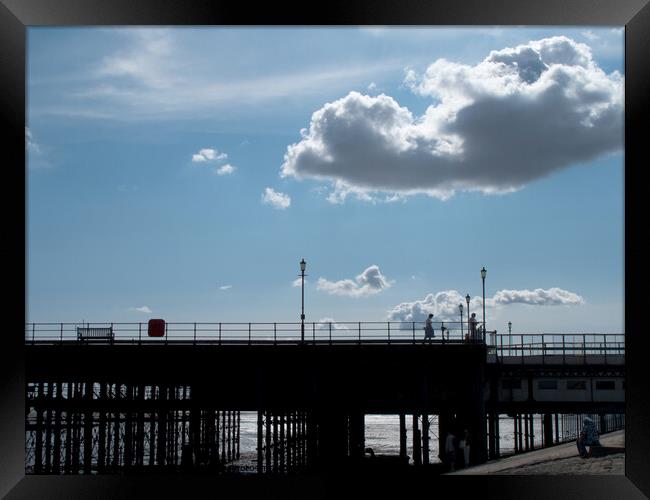 Part of the walkway in silhouette at Southend Pier, Essex, UK, with isolated clouds overhead. Framed Print by Peter Bolton