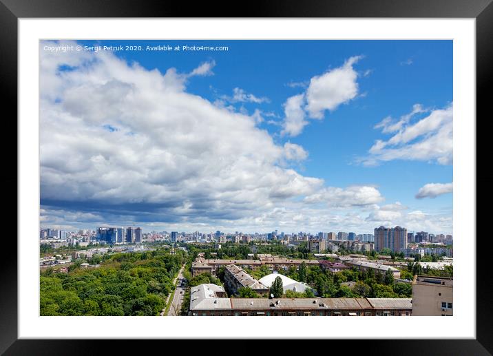 A cityscape with a green park in an old residential area of the city and new buildings on the horizon against a bright blue sky with thickening clouds. Framed Mounted Print by Sergii Petruk