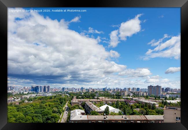A cityscape with a green park in an old residential area of the city and new buildings on the horizon against a bright blue sky with thickening clouds. Framed Print by Sergii Petruk