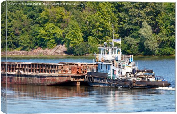 An old river tug pushes an empty barge ahead of itself along the river bank. Canvas Print by Sergii Petruk