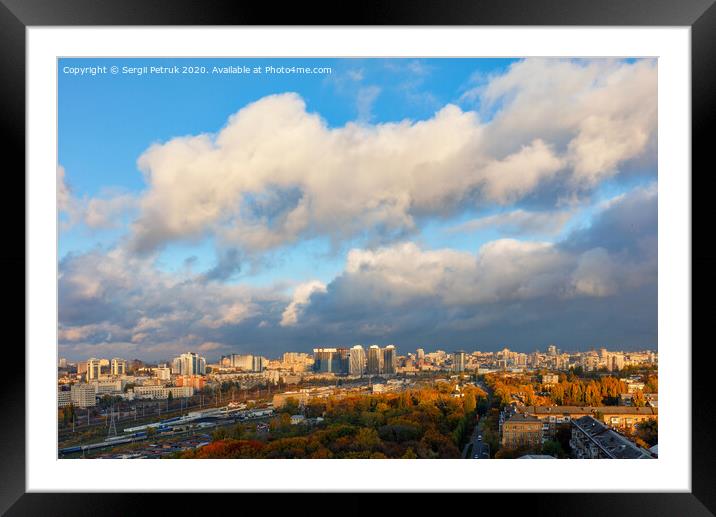 The colorful cityscape of autumn Kyiv, the sun's rays from behind gray clouds catch and brightly illuminate the orange foliage of the city park. Framed Mounted Print by Sergii Petruk