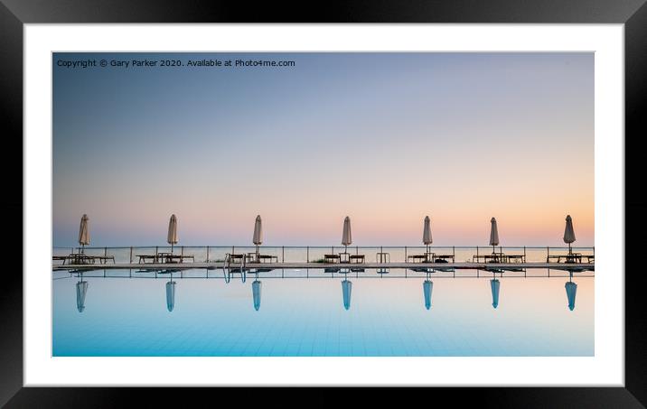 row of sunbeds and sun shades, reflecting in a still swimming pool, as the sun sets, in the Mediterranean	 Framed Mounted Print by Gary Parker