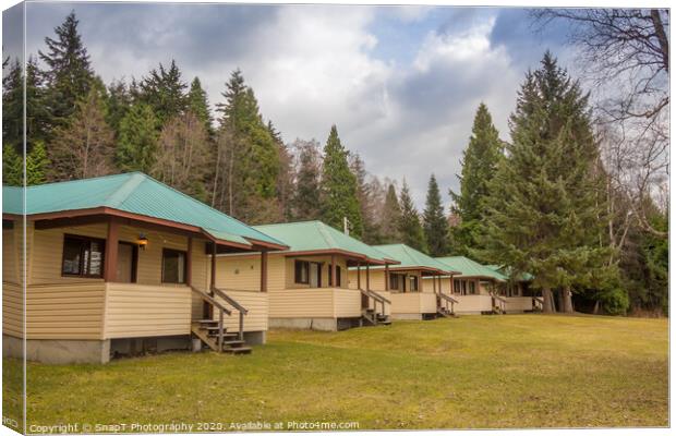 A row of cabins set in woodland with dark clouds above Canvas Print by SnapT Photography