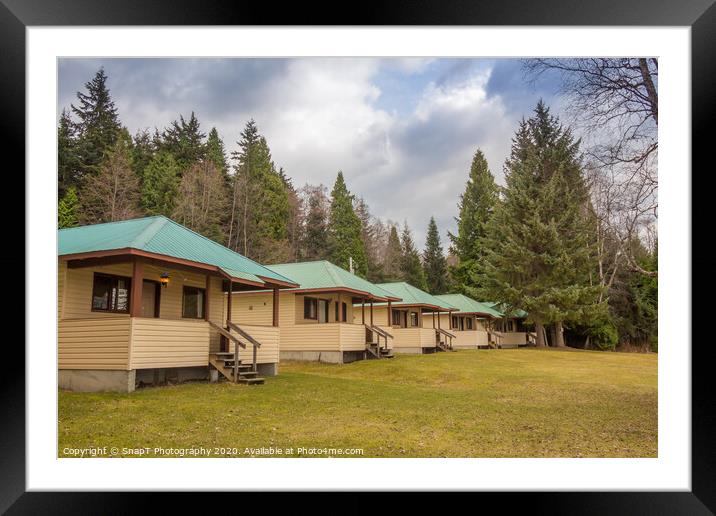 A row of cabins set in woodland with dark clouds above Framed Mounted Print by SnapT Photography
