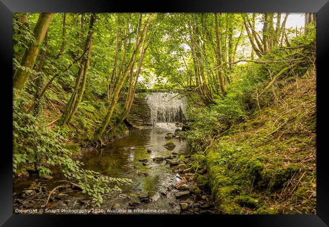 Water flowing over an old weir and through a woodland, over stones Framed Print by SnapT Photography