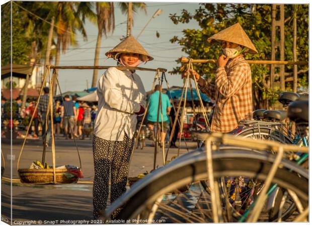 Two Vietnamese women with conical hats, carrying shoulder poles by a river in the afternoon Canvas Print by SnapT Photography