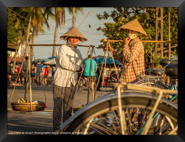 Two Vietnamese women with conical hats, carrying shoulder poles by a river in the afternoon Framed Print by SnapT Photography