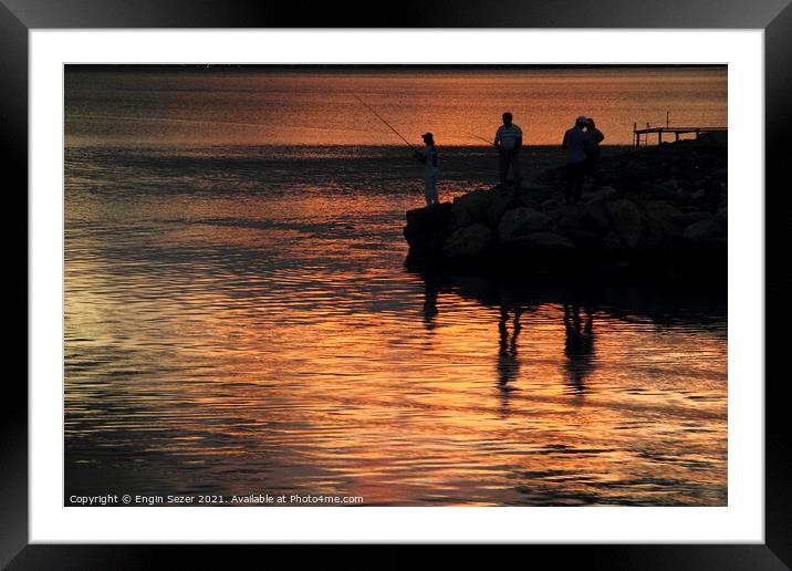 Silhouette of fishing people standing next to a bo Framed Mounted Print by Engin Sezer