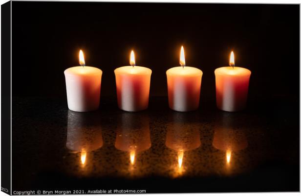 Four burning candles with reflections Canvas Print by Bryn Morgan