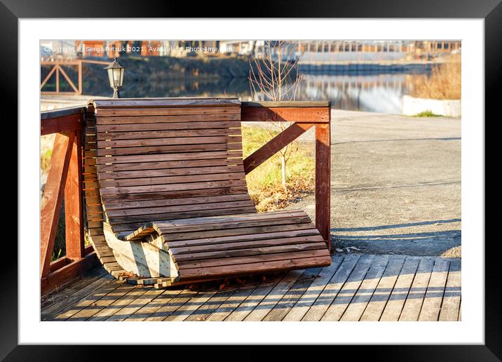 Outdoor furniture, a wooden chair on the river bank is illuminated by the rays of the bright sun against the background of the calm smooth surface of the water in blur. Framed Mounted Print by Sergii Petruk