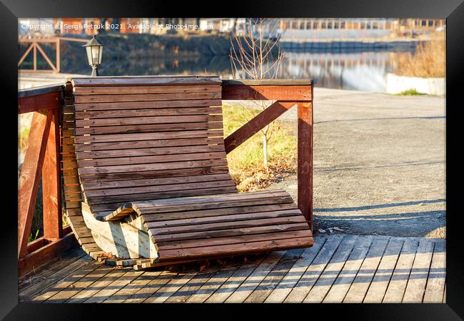 Outdoor furniture, a wooden chair on the river bank is illuminated by the rays of the bright sun against the background of the calm smooth surface of the water in blur. Framed Print by Sergii Petruk
