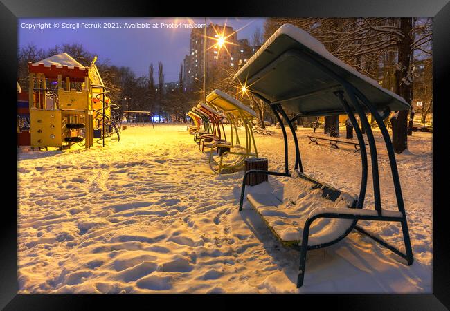 Wooden benches and a playground in the winter city evening park are covered with snow against the background of blue twilight. Framed Print by Sergii Petruk