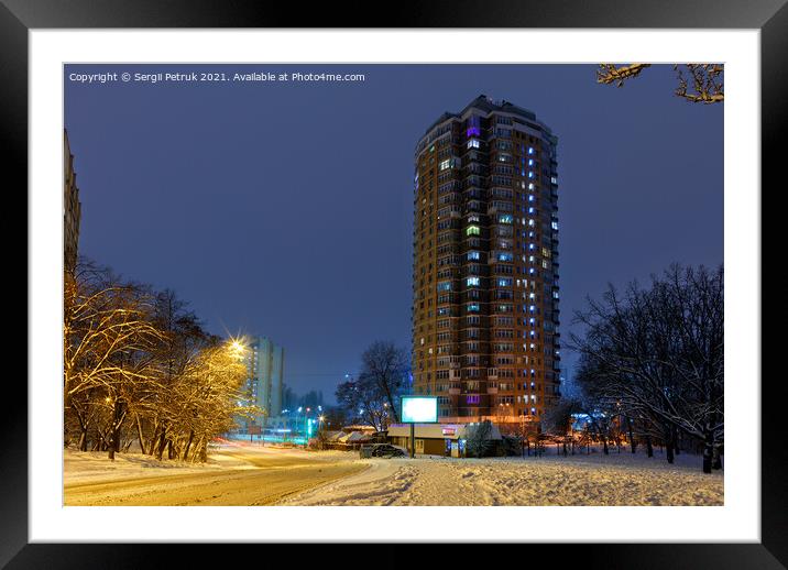 High-rise apartment building against the background of a city street in a winter city evening park covered with snow against a background of blue twilight. Framed Mounted Print by Sergii Petruk