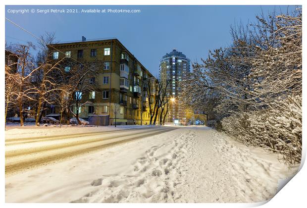 Snow-covered road along a city street with trees in the snow and city evening lighting against the backdrop of blue twilight. Print by Sergii Petruk