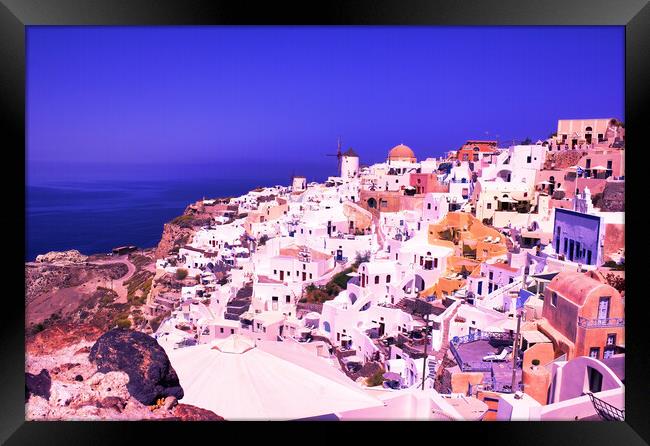 Santorini, Greece: Beautiful city of Oia ( Ia ) on a hill of white houses with blue roof and windmills against dramatic pink sky, located in Greek Cyclades islands in Mediterranean sea Framed Print by Arpan Bhatia