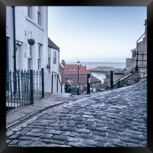 Whitby town cobbled streets and sea view Framed Print by Stuart Chard