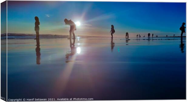 Silhouetted people in a row on a wet sand beach. Canvas Print by Hanif Setiawan