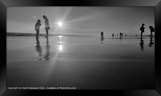 Silhouetted people in a row on a wet sand beach. Framed Print by Hanif Setiawan
