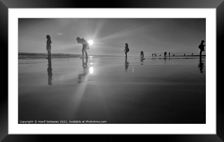 Silhouetted people in a row on a wet sand beach. Framed Mounted Print by Hanif Setiawan