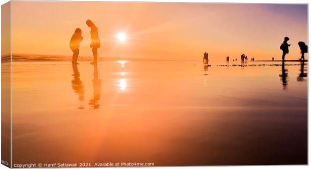 Silhouetted people in a row on a wet sand beach. Canvas Print by Hanif Setiawan