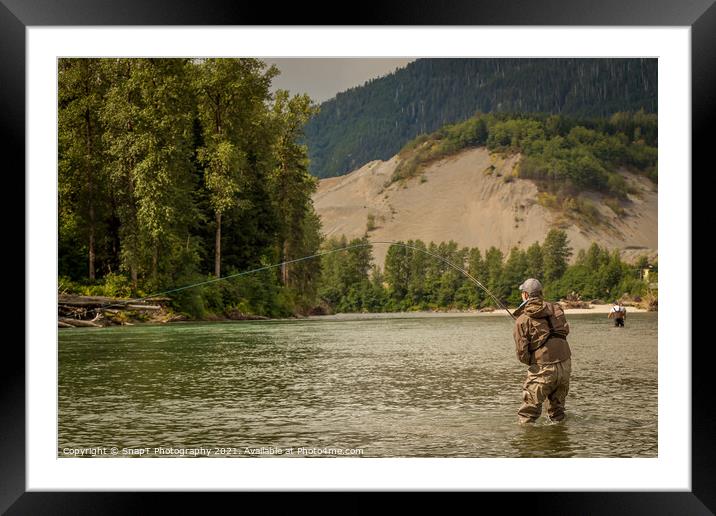 A fly fisherman hooked into a fish on a river with mountains and trees in the background Framed Mounted Print by SnapT Photography