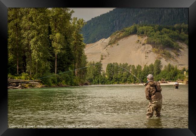 A fly fisherman hooked into a fish on a river with mountains and trees in the background Framed Print by SnapT Photography