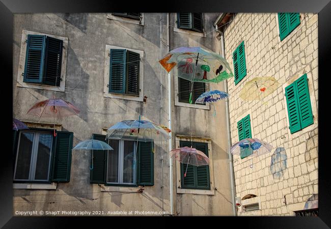 Flying umbrellas in a square in the old town of Kotor, in Montenegro Framed Print by SnapT Photography