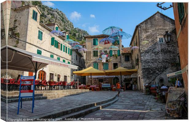 Cafe's and flying umbrellas on a square in the old town of Kotor, Montenegro Canvas Print by SnapT Photography