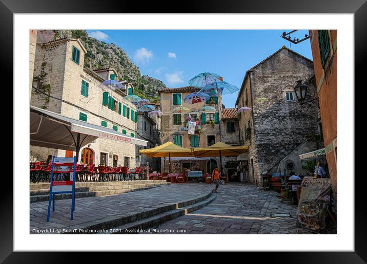 Cafe's and flying umbrellas on a square in the old town of Kotor, Montenegro Framed Mounted Print by SnapT Photography