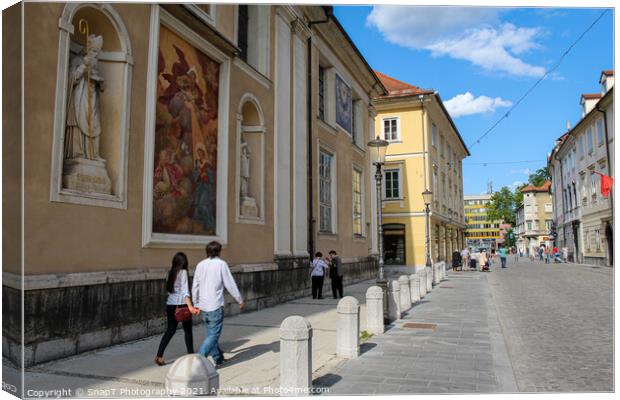 Tourists walking past the art on the wall at Ljubljana Cathedral, Slovenia Canvas Print by SnapT Photography