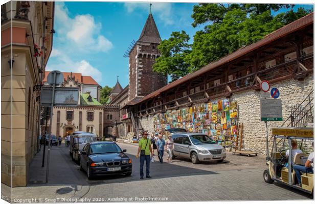 Artists pictures displayed on the wall of St. Florian's Gate on Pijarska Street, old town of Krakow, Poland Canvas Print by SnapT Photography