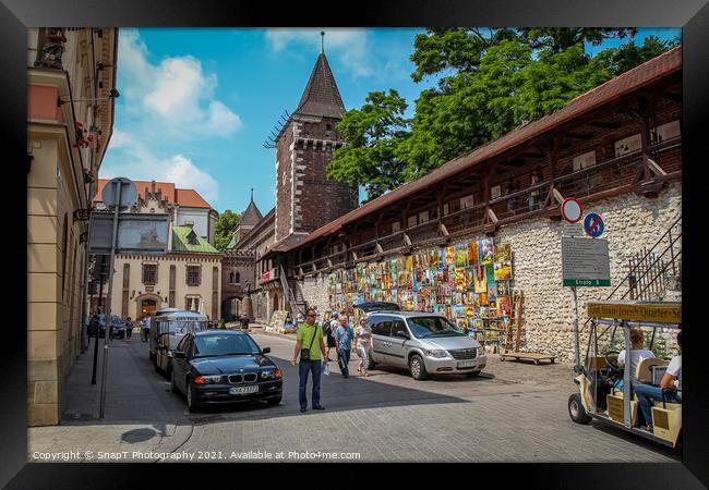 Artists pictures displayed on the wall of St. Florian's Gate on Pijarska Street, old town of Krakow, Poland Framed Print by SnapT Photography