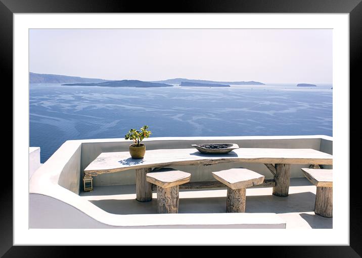 Santorini, Greece: A pot with flower or plant and a plate on a wooden table with wooden chair against beautiful sea ocean background with mountains Framed Mounted Print by Arpan Bhatia