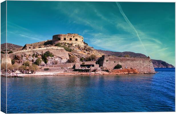 Crete, Greece: Wide angle view of Spinalonga unhabited island with a 16th century venetian fortress and the ruins of a formar leper colony against cloudy blue sky and blue water in the foreground Canvas Print by Arpan Bhatia
