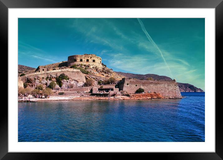 Crete, Greece: Wide angle view of Spinalonga unhabited island with a 16th century venetian fortress and the ruins of a formar leper colony against cloudy blue sky and blue water in the foreground Framed Mounted Print by Arpan Bhatia