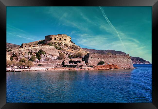 Crete, Greece: Wide angle view of Spinalonga unhabited island with a 16th century venetian fortress and the ruins of a formar leper colony against cloudy blue sky and blue water in the foreground Framed Print by Arpan Bhatia
