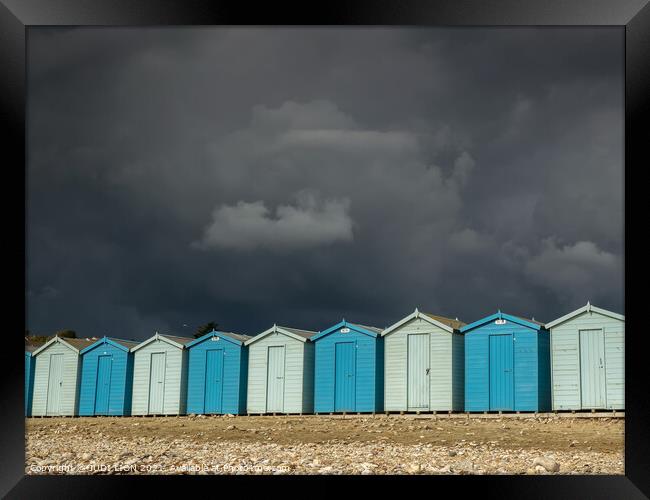Blue beach huts under a black sky Framed Print by JUDI LION