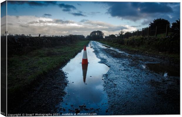 A red traffic cone reflecting a pot hole containing a pool of water on a road Canvas Print by SnapT Photography