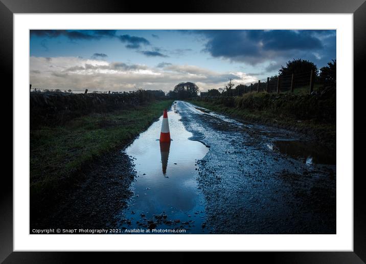 A red traffic cone reflecting a pot hole containing a pool of water on a road Framed Mounted Print by SnapT Photography