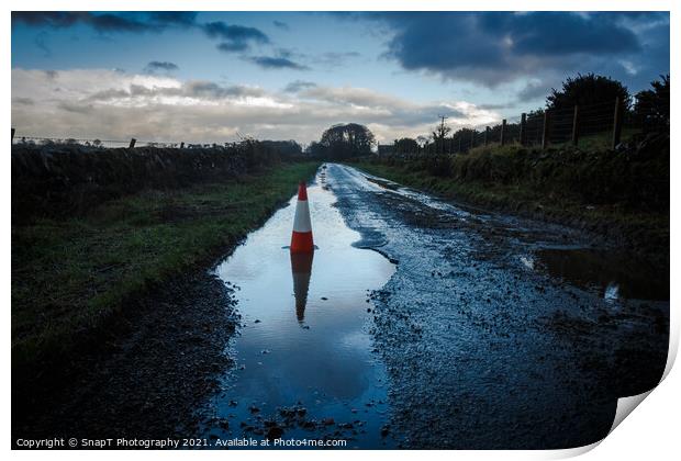 A red traffic cone reflecting a pot hole containing a pool of water on a road Print by SnapT Photography