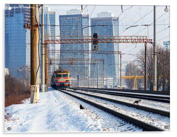 An old electric train moves on rails against the backdrop of a cityscape of skyscrapers on a sunny winter day. Acrylic by Sergii Petruk