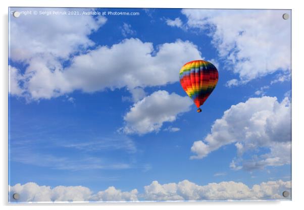 A motley multicolored hot air balloon raises a basket with tourists in the blue sky among white clouds. Acrylic by Sergii Petruk