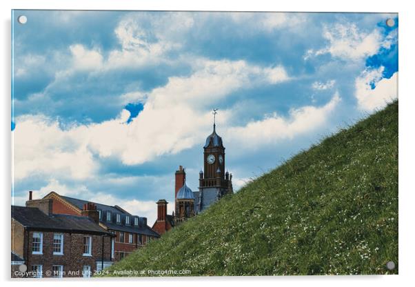 Quaint European town with historic buildings and a clock tower, set against a vibrant blue sky with fluffy clouds, and a lush green hill in the foreground in York, North Yorkshire, England. Acrylic by Man And Life