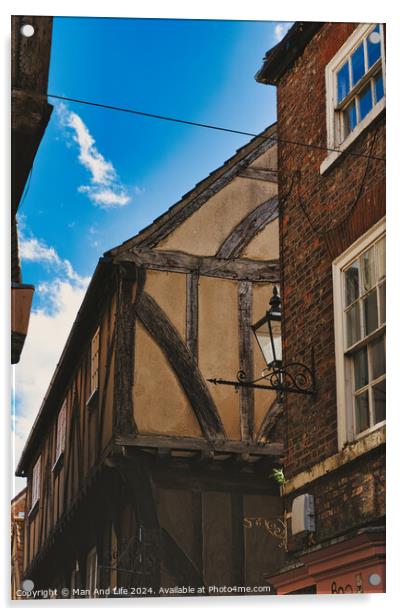Quaint half-timbered building with exposed wooden beams under a clear blue sky, showcasing traditional architectural details and a vintage street lamp in York, North Yorkshire, England. Acrylic by Man And Life