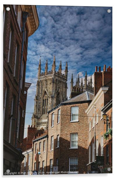Quaint cobbled street leading to a majestic Gothic cathedral under a blue sky with wispy clouds, showcasing historical architecture and urban charm in York, North Yorkshire, England. Acrylic by Man And Life