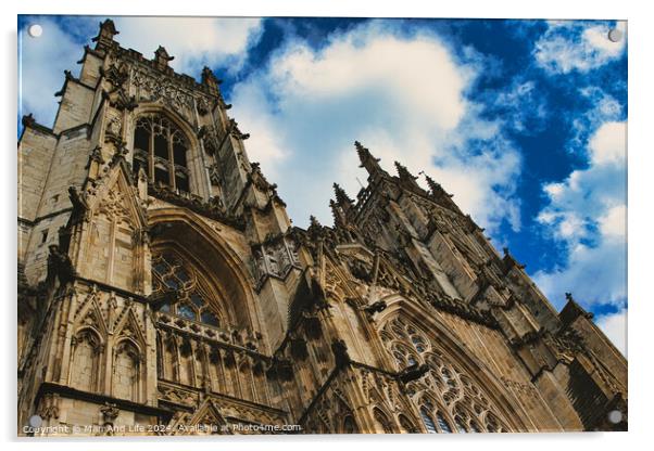 Dramatic angle of a Gothic cathedral's facade with intricate stone carvings against a vivid blue sky with fluffy clouds, showcasing architectural grandeur and historical elegance in York, North Yorkshire, England. Acrylic by Man And Life