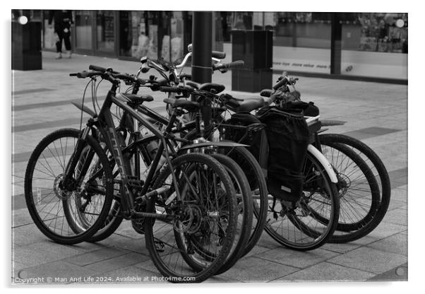 Black and white image of multiple bicycles locked to a bike rack in an urban setting, with a blurred background of a city street Acrylic by Man And Life