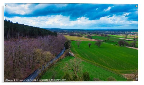 Aerial view of a vibrant rural landscape with a road running alongside a forest, contrasting green fields and a dramatic cloudy sky. Acrylic by Man And Life