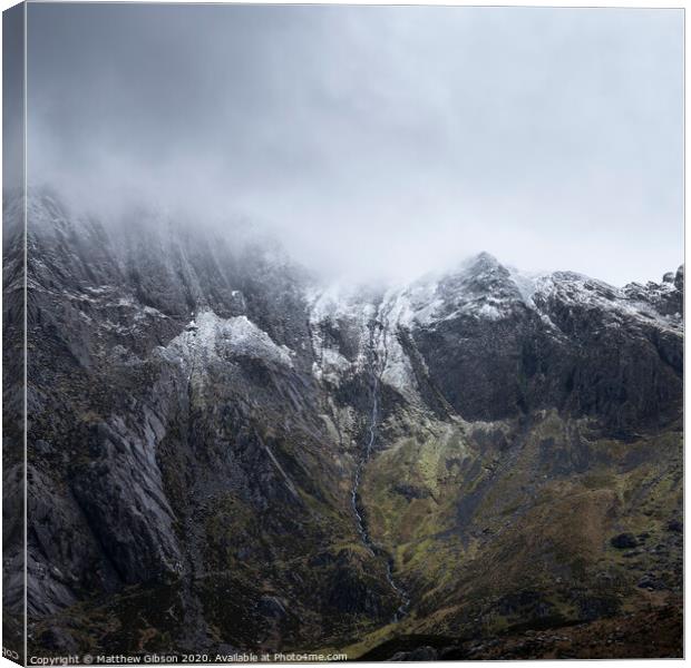 Stunning dramatic landscape image of snowcapped Glyders mountain range in Snowdonia during Winter with menacing low clouds hanging at the peaks Canvas Print by Matthew Gibson