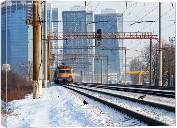An old electric train moves on rails against the backdrop of a cityscape of skyscrapers on a sunny winter day. Canvas Print by Sergii Petruk